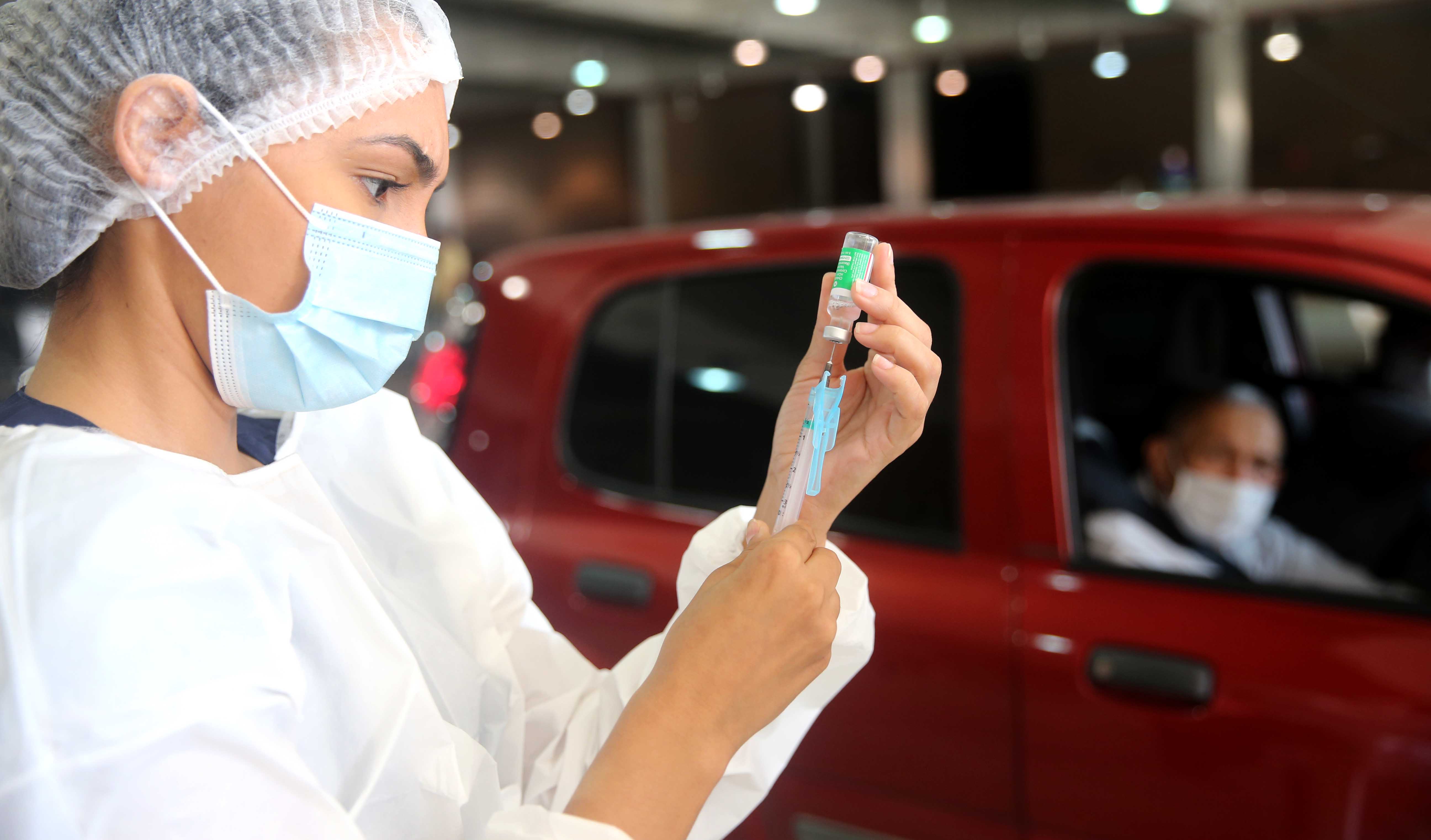 enfermeira prepara uma seringa de vacina enquanto é observada por um senhor dentro do carro